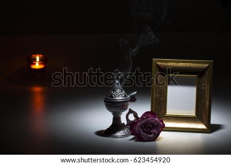 blank gilded picture frame with thurible and candle flame and pink rose on dark 