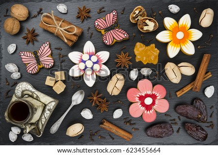 Gingerbread cookies with cup of coffee, nuts, dates and spices, colorful homemade cakes in shape of flower and butterfly on black textured background, top view 