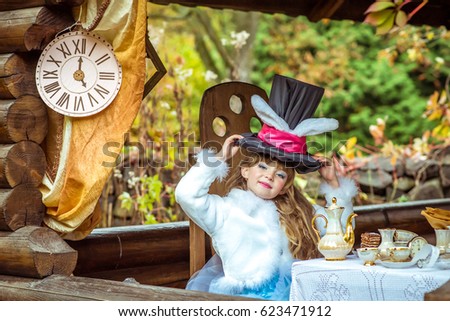 An little beautiful girl in the scenery holding cylinder hat with ears like a rabbit over head at the table in the garden