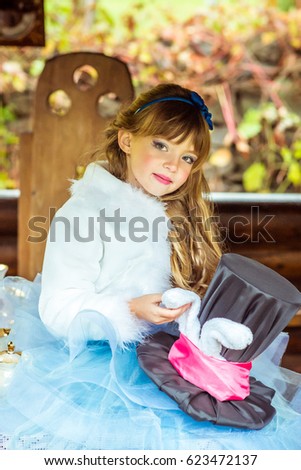 An little beautiful girl in the scenery holding cylinder hat with ears like a rabbit in the hands at the table in the garden