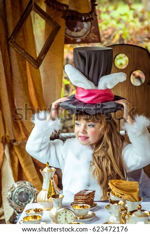 An little beautiful girl in the scenery holding cylinder hat with ears like a rabbit over head at the table in the garden