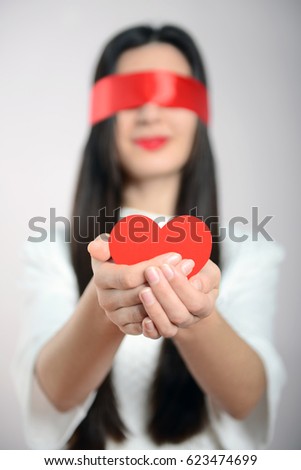 A young girl with blindfolded eyes and a heart in her hands. Love is blind