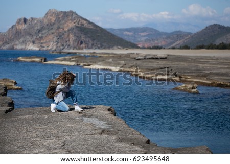 Young woman wearing jeans gray jacket and backpack standing and photographing rock ribbed beach in Gazipasha Alanya Turkey famous for its lagoons