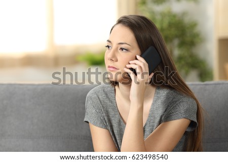 Serious woman attending a phone call sitting on a sofa in the living room at home Royalty-Free Stock Photo #623498540