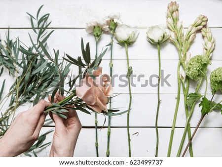 florist's hands making bouquet on white wood background