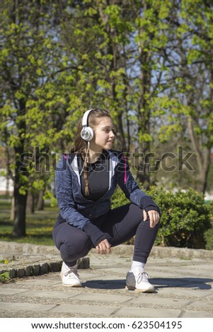 Beautiful young woman doing exercises and enjoys listening to music in the park. Selective focus and small depth of field.