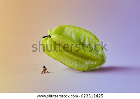 Microworld with woman figure under the carambola tropical fruit on green pink background. Cartoon style, food photography