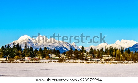 The snow covered peaks of the Golden Ears mountain and Mount Robie Reid behind the town of Fort Langley in the Fraser Valley of British Columbia, Canada on a cold winter day and snow covered fields Royalty-Free Stock Photo #623575994