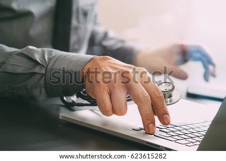 close up of smart medical doctor working with laptop computer and stethoscope on dark wooden desk 