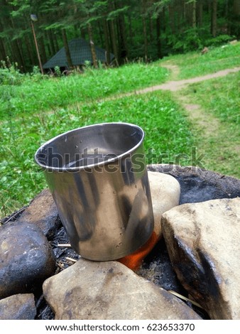 In the woods on the rocks a metal cup with water on fire