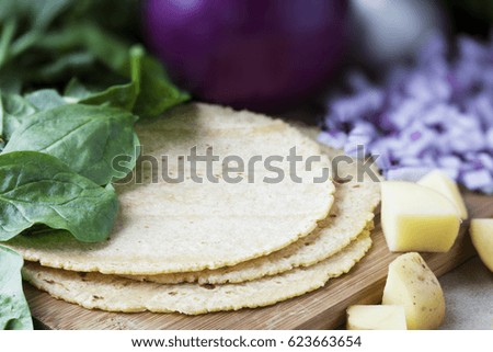 Corn tortillas surrounded by spinach, onions, and potatoes.  Ingredients for making vegan tacos.
