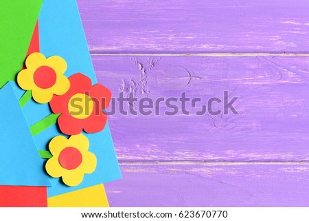 Colourful paper flowers, paper sheets on purple wooden background with copy empty space for text. Bright flowers card. Summer or spring backdrop