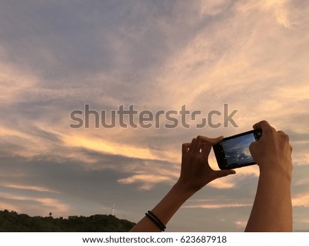 a woman takes a picture of the beautiful twilight sky by her mobile phone with far away white windmill on the top of the hill background on her great holiday