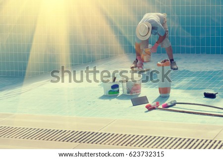 Man in a hat put the tiles on the bottom of the poolin the sunlight . Toned Royalty-Free Stock Photo #623732315