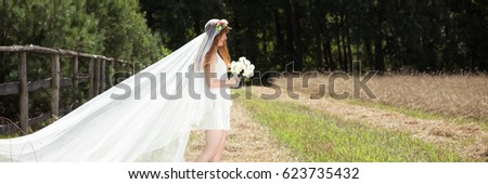 Young bride with long, white veil standing in the country area