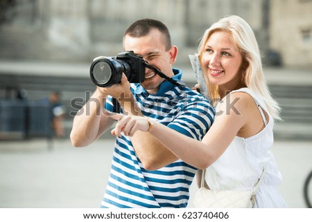 Two cheerful tourists holding camera in hands and photographing in city