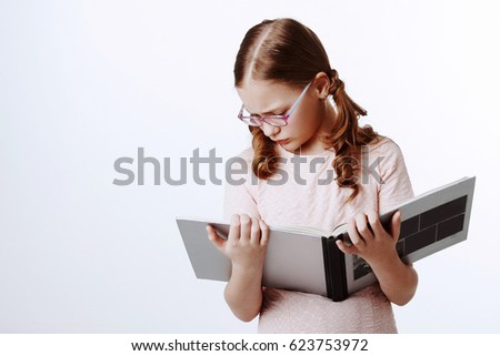 Portrait of a teenage girl with long hair in glasses and with a book on a white isolated background.