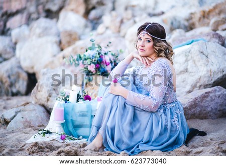 Beautiful young woman waiting by the sea. Bride in the wedding gown with bouquet