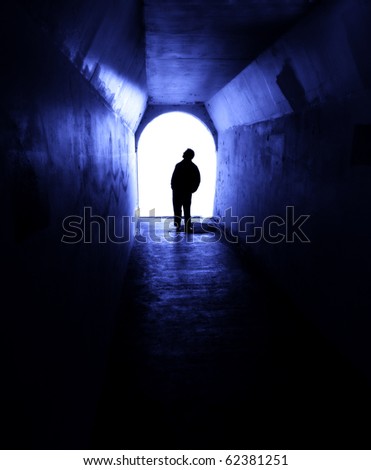 Person in long tunnel walkway with white light at the end
