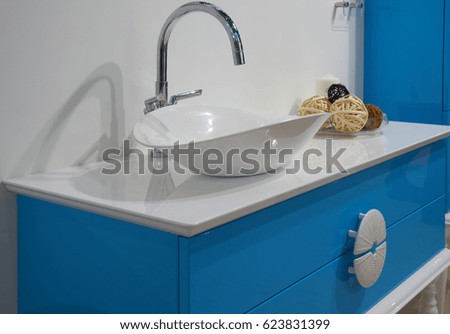 White top ceramic washbasin, glossy metal mixer and blue bathroom furniture