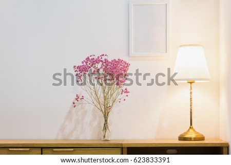 Pink flower bouquet in a glass bottle and brass desk lamp on top of a wooden sideboard in a white living room