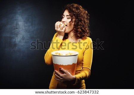 Greedy woman grabs handful of popcorn with eyes closed 
