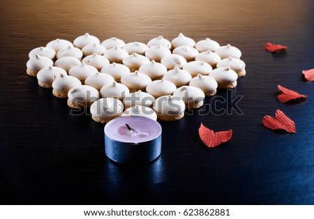Small cookies laid in the shape of heart with red paper hearts on black background. Selective focus. Shallow depth of field.