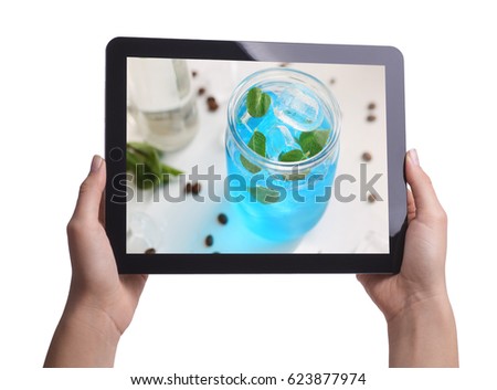 A woman holding a tablet in her hand with an image of an alcoholic cocktail on the display
