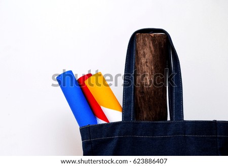 Denim bags, paper three primary colors red, yellow, blue, hanging on a wooden pole. Hat with red flowers in the picture with a white backdrop.