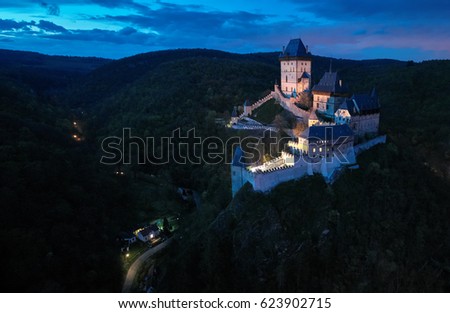 Aerial, night view on Karlstejn Castle, Burg Karlstein, large Gothic castle near Prague  illuminated by floodlights. Picturesque Czech castle on the hilltop against starry dark blue sky. Aerial photo.