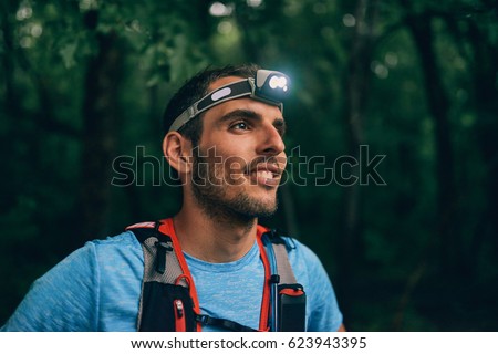Fit male jogger with a headlamp rests during training for cross country trail race in nature park. Royalty-Free Stock Photo #623943395