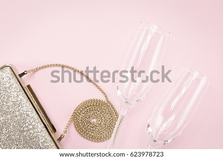 Festive evening golden clutch and two champagne glasses on pink. Holiday and celebration background. Luxury accessories and party concept. Horizontal