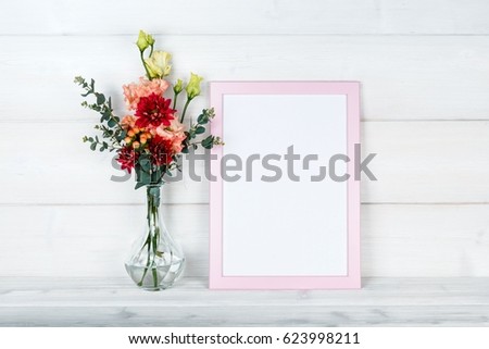 Pink flowers in vase and a photo frame on a wooden background. Mockup with copyspace.