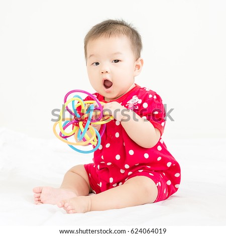 Portrait of a little adorable infant baby girl sitting on the bed and smiling to camera with bites toy