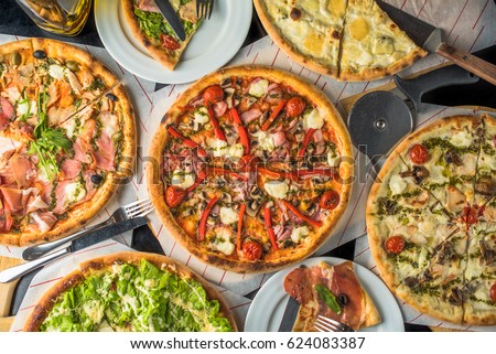 Pizza on paper on a wooden board and pieces of pizza in plates. A lot of pizza on a black table close up. Healthy hot food. Royalty-Free Stock Photo #624083387