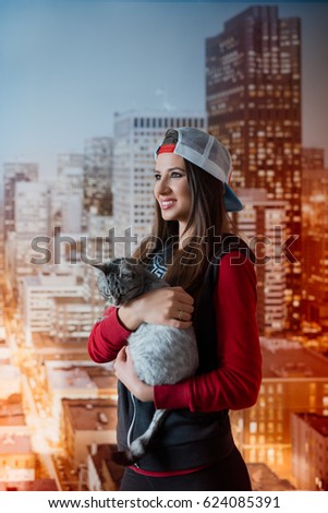 Vertical portrait of young smiling girl, with white cap, holding a shorthair cat in hands. 