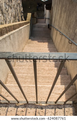 Steps down in old antique castle with metal bar that forbids entry. The concept of protection, prohibition, caution and protection. Vertical perspective down from light to dark, in depth.