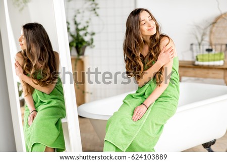 Portarit of a young woman in green towel relaxing on the bathtub at the comfortable bathroom