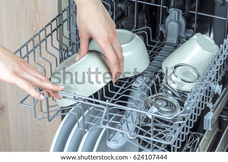 Unloading clean dishes from the dishwasher machine. Focus on hands.