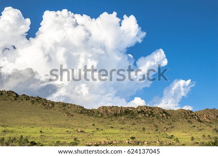 Lurking clouds on a blue summer sun sky creeping over rocky green hills