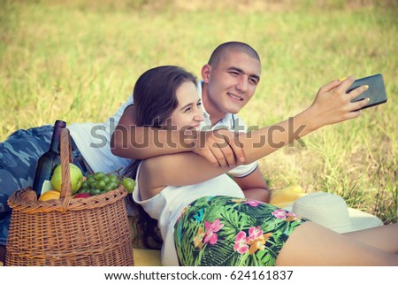 Happy couple making selfie with smart phone on picnic. Smiling Caucasian couple having fun in a meadow and taking selfie.