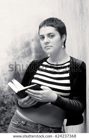 A girl with big eyes and short hair reads a book, standing by the wall. Preparing for exams at the university. Close-up portrait. Black and white photo.