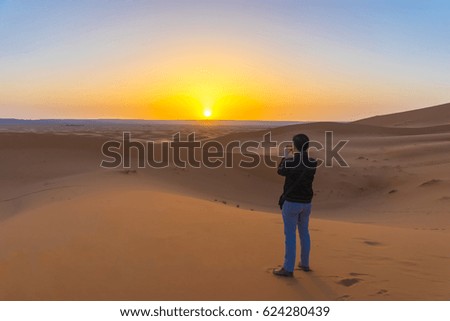 A traveller is taking photo of the sunrise on the sand dunes at Sahara desert near the Merzougha in Morocco