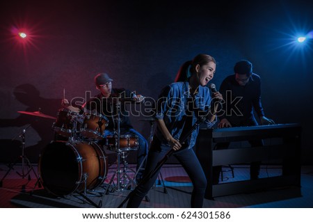 Musician band hand holding the microphone and singing a song and playing music instrument with Fellow band musicians on black background with spot light and lens flare, musical concept