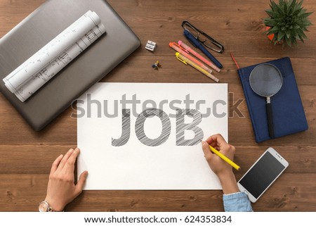 The girl sits at the table with a mobile phone, a laptop, business accessories and a sheet with text Job