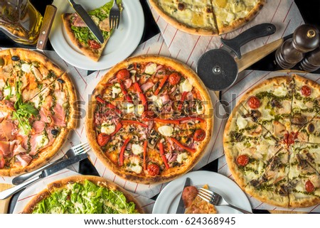 Pizza on paper on a wooden board and pieces of pizza in plates. A lot of pizza on a black table close up. Healthy hot food. Royalty-Free Stock Photo #624368945