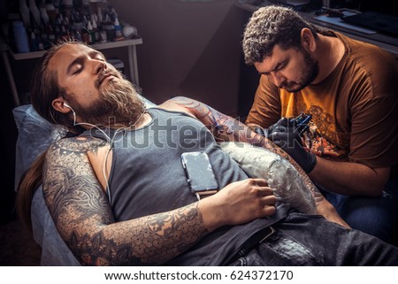 Master makes tattoo pictures in tattoo studio./Tattoo specialist works in tatoo salon.