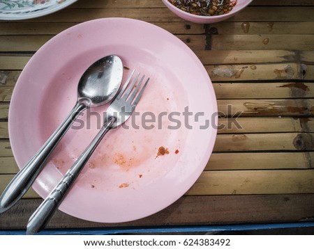 Pink plastic dish, spoon and fork steel are table wooden with copy space and top view., Food was eaten, But grease and food particles stick to the dish., enjoy with thai food.