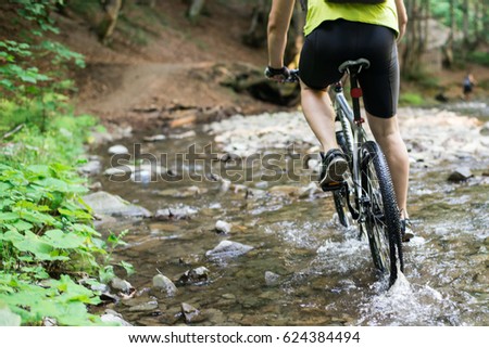 Mountain biker speeding through forest stream. Water splash.