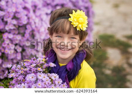 Cute smiling girl wearing colorful clothes enjoying time together close to purple flowers in rubber shoes with yellow balloons. 